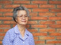 Elderly Asian woman looking at camera and smiling while standing with brick wall background Royalty Free Stock Photo