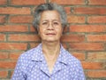 Asian elderly woman looking at camera and smiling while standing with brick wall background Royalty Free Stock Photo