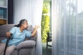 Asian elderly woman Which holds the cane to support, Sitting absent lonely on the sofa and looking outside the door Royalty Free Stock Photo