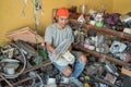 Asian electronics repairman holding fan while sitting around broken items