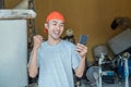 The Asian electronics repairman with a pleasant surprised gesture looks at the smartphone screen