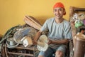 Asian electronics repairman smiles at the camera while holding the fan while sitting around broken items