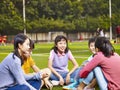 Asian elementary schoolchildren sitting and chatting on grass in Royalty Free Stock Photo