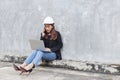 Asian engineer developer woman wear black suit and white safety hardhat using laptop and talking mobile phone working onsite.