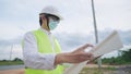 Asian engineer employee wear safety vest helmet looking at construction planner on wireles tablet on outdoor site, civil Engineer