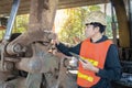 Asian engineer wearing hard hat and protective vest is inspecting machine while standing and holding tablet with serious face, Royalty Free Stock Photo