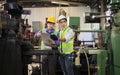 Asian engineering manager and mechanic worker in safety hard hat and reflective cloth using lathe machine inside the factory Royalty Free Stock Photo