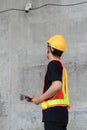 Asian engineering worker wearing hard hat and protective vest using tablet to check in closed-circuit camera in construction site Royalty Free Stock Photo