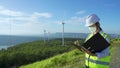 Asian engineers or technican woman with mask and white helmet are checking the wind turbine system with document at renewable