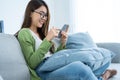 Asian excited young woman winner feeling happy while looking at phone. Attractive girl student sit on sofa in living room and Royalty Free Stock Photo