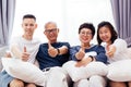 Asian family with adult children and senior parents giving thumbs up and relaxing on a sofa at home together.