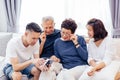 Asian family with adult children and senior parents using a mobile phone and relaxing on a sofa at home together.