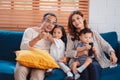 Asian family consisting of parents, happy son and daughter watching TV or movie together on sofa in living room at home. enjoy Royalty Free Stock Photo