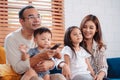 Asian family consisting of parents, happy son and daughter watching TV or movie together on sofa in living room at home. enjoy Royalty Free Stock Photo