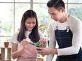 Asian family couple look after their horticultural business planting in glasshouse. Young man holds small tree pot Royalty Free Stock Photo