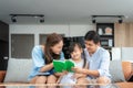 Asian family with father, mother and her daughter reading fairy tail story book on sofa at home together and pointing on the book Royalty Free Stock Photo