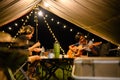 Asian family and friends vacation camp, Dinner and relaxing guitar play under tarp or flysheet, Outdoor camping on the courtyard