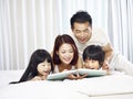 Asian family with two children reading book in bed Royalty Free Stock Photo