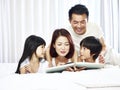 Asian couple and two children reading book together in bed Royalty Free Stock Photo