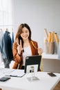 Fashion designer woman talking smart phone and using laptop with digital tablet computer in modern studio the clothes hanging on Royalty Free Stock Photo