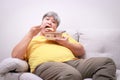 Asian fat man sits and eats food on the sofa happily.