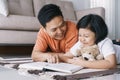 Asian father and daughter are reading book while lying on the carpet in the living room at her home. The cute little girl hugs the