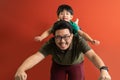 Asian father giving son ride on the back with a red background. Portrait of a happy father giving son piggyback a ride on his Royalty Free Stock Photo