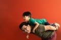 Asian father giving son ride on the back with a red background. Portrait of a happy father giving son piggyback a ride on his Royalty Free Stock Photo