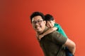 Asian father giving son ride on the back with a red background. Portrait of a happy father giving son piggyback a ride on his Royalty Free Stock Photo