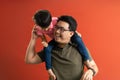 Asian father giving son ride on the back with a red background. Portrait of a happy father giving son piggyback a ride on his Royalty Free Stock Photo