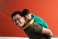 Asian father giving son ride on the back with a red background. Portrait of a happy father giving son piggyback a ride on his Royalty Free Stock Photo