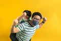 Asian father giving son ride on the back with a yellow background. Portrait of a happy father giving son piggyback a ride on his Royalty Free Stock Photo