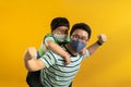 Asian father giving son ride on the back with a yellow background. Portrait of a happy father giving son piggyback a ride on his Royalty Free Stock Photo