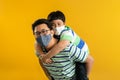 Asian father giving son ride on the back with a yellow background. Portrait of a happy father giving son piggyback a ride on his Royalty Free Stock Photo