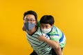 Asian father giving son ride on the back with a yellow background. Portrait of a happy father giving son piggyback a ride on his Royalty Free Stock Photo