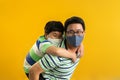 Asian father giving son ride on the back with a yellow background. Portrait of a happy father giving son piggyback a ride on his Royalty Free Stock Photo