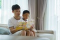 Asian father holds a book to teach his children to read on the sofa in the living room, fathers interact with their children