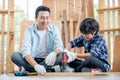 Asian father look carefully son use drill in their workplace of carpentering with happy emotion. Asian family concept to stay at
