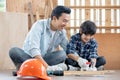 Asian father look carefully son use hammer to hopnailed in their workplace of carpentering with happy emotion. Asian family