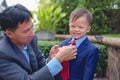 Asian father and son dressed in suits, Businessman helping his little child tying the necktie, Little kid looking and smiling at