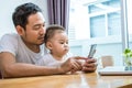 Asian father and son using smart phone together in home background. Technology and People concept. Lifestyles and Happy family th Royalty Free Stock Photo