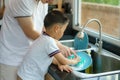 Asian father is teaching his son how to wash dishes, help with housework in the kitchen at home, fathers interact with their