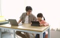Asian father working from home and caring his girl doing homework with digital table, Child using gadgets to study. Home schooling Royalty Free Stock Photo