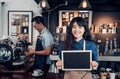 Asian female barista wear jean apron holding blank blackboard coffee menu at counter bar with colleague with smile face ,cafe