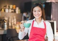 Asian female barista wear red apron holding hot cappuccino coffee cup menu at counter bar with smile face,cafe service concept Royalty Free Stock Photo