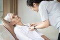 Asian female caregiver taking care of helping elderly patient get dressed,button on the shirt or changing clothes for a paralyzed