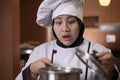 Asian female chef open cooking pot and smelling food aroma that she cooked, bad worried face expression