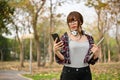 Asian female college student holding her laptop and using her phone while walking in park Royalty Free Stock Photo