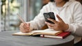 An Asian female college student using her smartphone while doing her homework at a cafe Royalty Free Stock Photo