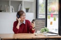 Asian female college student using laptop and phone with headphones while studying. Reading messages and greeting Royalty Free Stock Photo